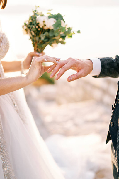 La novia con el ramo pone el anillo al dedo del novio. Cultivado. Sin rostro. Foto de alta calidad - Foto, Imagen
