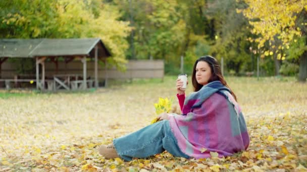 Sinfonia dei colori autunnali: nel cuore dell'autunno, una bella donna sorseggia tè caldo, avvolto in una sciarpa giallo sole. Filmati 4k di alta qualità - Filmati, video