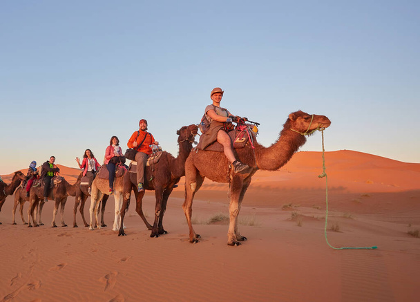 Turistas montando camellos, sonriendo, en el desierto del Sahara, Marruecos. - Foto, imagen
