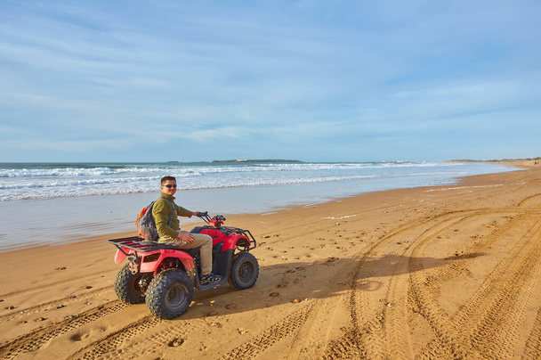 Egy fiatalember felfedezi az óceánt egy quad bike-on Essaouira közelében, megragadja egy kalandos utazás izgalmát a festői tengerparti tájon.. - Fotó, kép