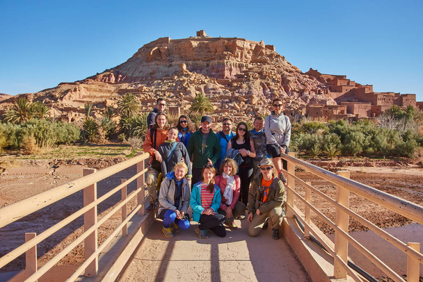 Turistas capturam um momento compartilhado, sorrindo e posando para uma foto de grupo contra o pano de fundo histórico da arquitetura antiga de Ait-Ben-Haddou - Foto, Imagem