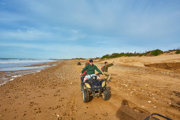 Група туристів насолоджується квадроциклом вздовж узбережжя Ессауїри, створюючи приголомшливе видовище на тлі мальовничого прибережного фону - Фото, зображення