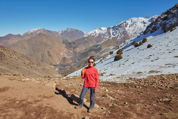 Atlas Dağları 'ndaki bir turist, arkasında karla kaplı tepelerle dağ manzarasının dingin güzelliğini yakalar.. - Fotoğraf, Görsel