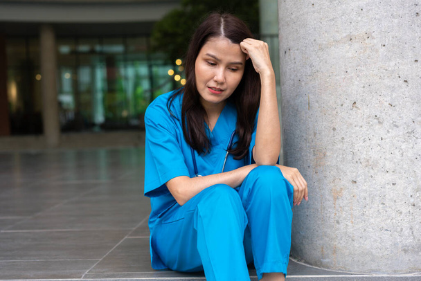 Stressaantuneen ja ylityöllistetyn naislääkärin muotokuva lääkäri istuu lattialla lähellä leikkaussalia sairaalassa ja riisuu naamion - Valokuva, kuva