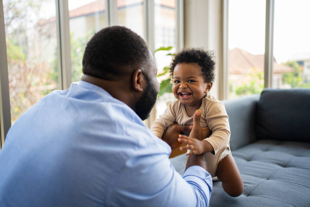 Портрет счастливого афроамериканского папы с симпатичной маленькой девочкой на диване дома в гостиной, заботливый отец улыбается и развлекает свою девочку, сидя на диване, счастливая семья - Фото, изображение