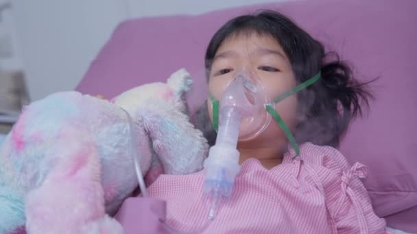 Una bambina asiatica ha una maschera di ossigeno e respira attraverso un nebulizzatore in ospedale. Concetto di bronchite, trattamento respiratorio e medico, medicina per inalazione, nebbia, da un nebulizzatore. - Filmati, video