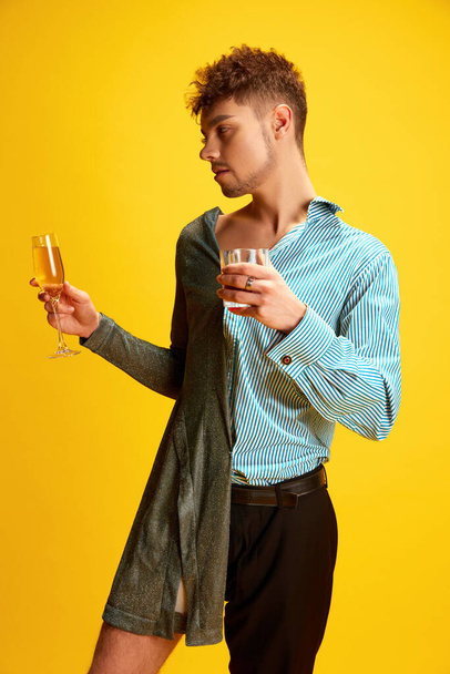 Rozlučka se svobodou a svobodou. Muž napůl oblečený v ženských a mužských šatech, pózující s brýlemi šampaňského a whisky v rukou na ženských a mužských stranách. Pojem sebevyjádření. Reklama - Fotografie, Obrázek