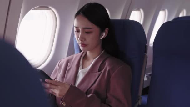Asyalı iş kadını uçuş sırasında kulaklık takarken telefonunu aktif olarak iş kaydını ve analizini yapmak için kullanıyor. O, görevlerine konsantre olur.,  - Video, Çekim