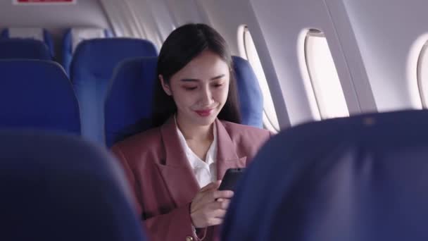 Een Aziatische zakenvrouw gebruikt haar telefoon om werk hartstochtelijk op te nemen en te analyseren tijdens het reizen in een vliegtuig. Ze beheert efficiënt haar taken tijdens de vlucht.  - Video