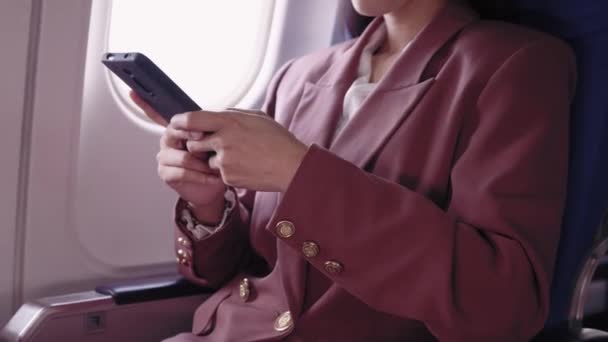 Eine asiatische Geschäftsfrau nutzt ihr Handy, um während einer Flugreise leidenschaftlich ihre Arbeit aufzuzeichnen und zu analysieren. Sie bewältigt ihre Aufgaben während des Fluges effizient.  - Filmmaterial, Video