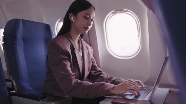 Une femme d'affaires asiatique travaille sur son ordinateur portable, enregistrant et analysant activement les tâches pendant son vol. Elle se consacre à maximiser la productivité pendant le transport - Séquence, vidéo