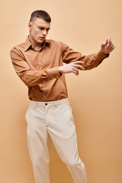 Porträt eines stilvollen, gut aussehenden Mannes im beigen Hemd, der die Hände auf einem pfirsichfarbenen beigen Hintergrund bewegt - Foto, Bild