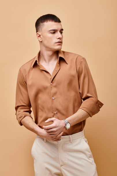 Portret van een stijlvolle knappe man in beige shirt die wegkijkt op een perziken beige achtergrond - Foto, afbeelding