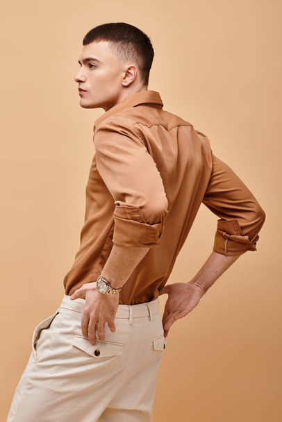 Back view portrait of stylish man in beige shirt with hand on pants on beige background - Photo, Image