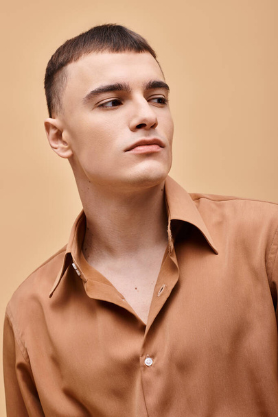Fashion portret van stijlvolle jongeman in beige shirt weg te kijken op perzikkleurige beige achtergrond - Foto, afbeelding