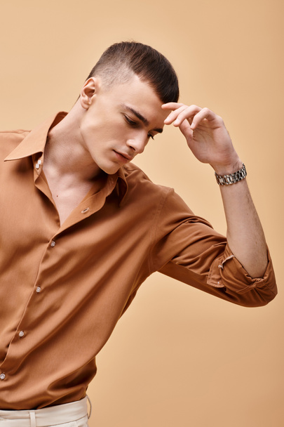 Portrait of young handsome man in beige shirt looking down on peachy beige background - Photo, Image