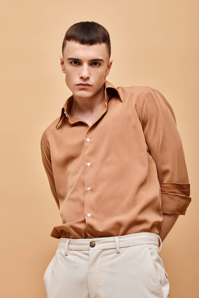 Portrait of handsome man in beige shirt with hands over his back on beige background - Foto, afbeelding