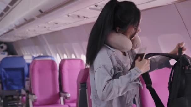 Aasialaisella naisturistilla on passi ja lentolippu, kun hän kävelee istuimelleen lentokoneessa, valmiina lomalle vapaapäivinään. Laadukas 4k kuvamateriaalia - Materiaali, video