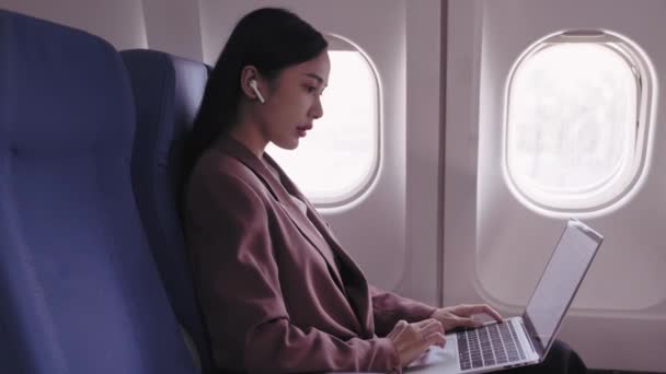 Eine asiatische Geschäftsfrau arbeitet an ihrem Laptop und zeichnet während ihres Fluges aktiv Aufgaben auf und analysiert sie. Sie widmet sich der Maximierung der Produktivität während der Fahrt - Filmmaterial, Video