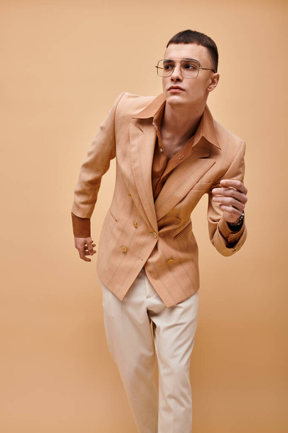 Портрет красивого чоловіка в бежевій куртці і окулярах позує на персиково-бежевому фоні - Фото, зображення