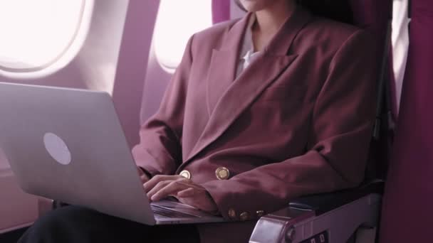 Een Aziatische zakenvrouw werkt aan haar laptop, die tijdens haar vlucht actief taken opneemt en analyseert. Ze is toegewijd aan het maximaliseren van de productiviteit tijdens het transport.  - Video