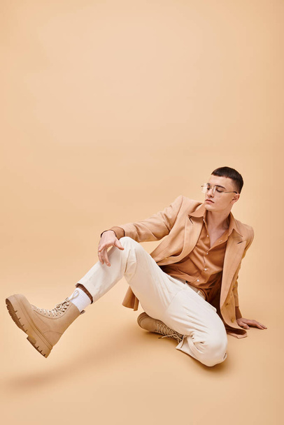 Tyylikäs mies 20s beige takki ja lasit istuu persikkainen beige tausta - Valokuva, kuva