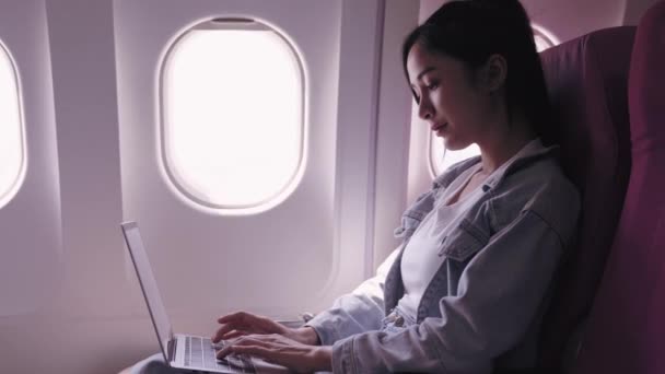 Ασιάτισσες ταξιδιώτες, επί του παρόντος σε ένα ταξίδι με αεροπλάνο, εργάζονται επιμελώς σε φορητούς υπολογιστές τους με εστίαση και αποφασιστικότητα. επίδειξη της σκόπιμης και αφοσιωμένης εργασίας  - Πλάνα, βίντεο