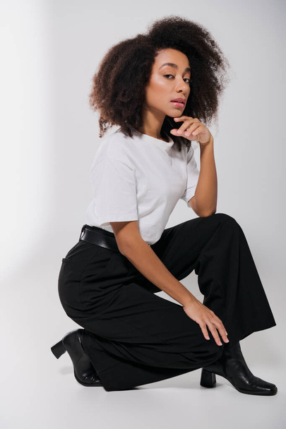 bel modello afro-americano femminile seduto sul pavimento e guardando la fotocamera, concetto di moda - Foto, immagini