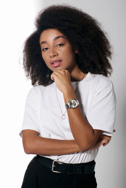 belle femme afro-américaine en tenue chic avec des cheveux bouclés en regardant la caméra, concept de mode - Photo, image