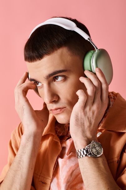 Retrato pf hombre con estilo con auriculares inalámbricos escuchando música sobre fondo rosa - Foto, imagen