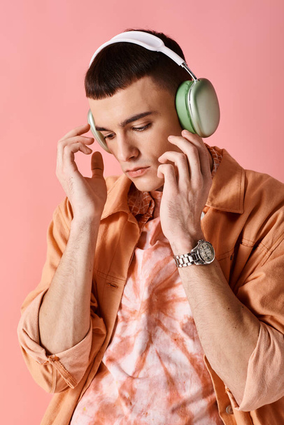 Hombre guapo con auriculares inalámbricos escuchando música sobre fondo rosa mirando hacia abajo - Foto, Imagen