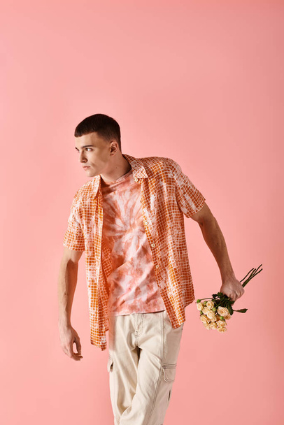 Портрет стильного молодого человека в многослойном наряде с цветами на розовом фоне - Фото, изображение