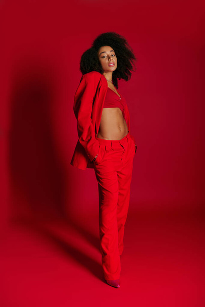 atraente sedutor mulher afro-americana em trajes vibrantes olhando para a câmera no fundo vermelho - Foto, Imagem