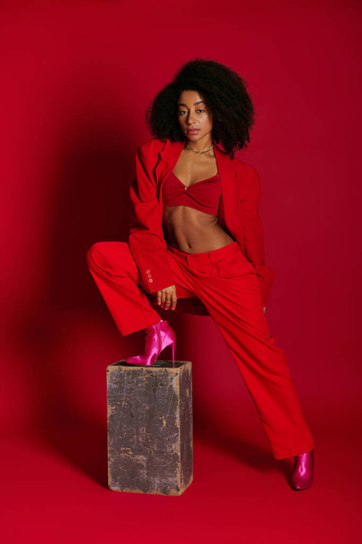 dość modny afrykański amerykański kobieta model w sexy strój patrząc na aparat na czerwonym tle - Zdjęcie, obraz