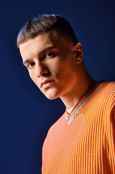 Portrait de mode d'un bel homme en chemise orange et short blanc posant sur fond bleu foncé - Photo, image