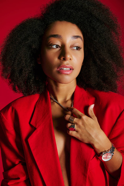 приваблива афро-американська жіноча модель в червоному блістері, дивиться на червоний фон, концепція моди - Фото, зображення
