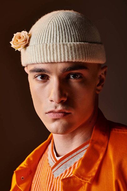 Portret stylowego mężczyzny w pomarańczowym stroju w beżowej czapce z kwiatem patrzącego w kamerę - Zdjęcie, obraz