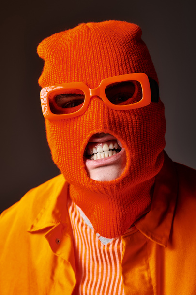 Vihainen mies oranssi asu yllään balaclava kasvonaamio oranssi aurinkolasit ja näyttää hampaat - Valokuva, kuva