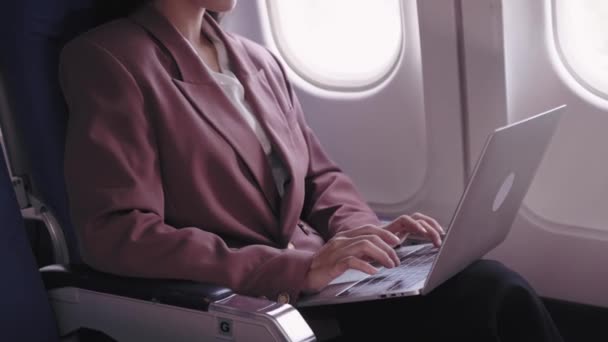 Une femme d'affaires asiatique travaille sur son ordinateur portable, enregistrant et analysant activement les tâches pendant son vol. Elle se consacre à maximiser la productivité pendant le transport - Séquence, vidéo