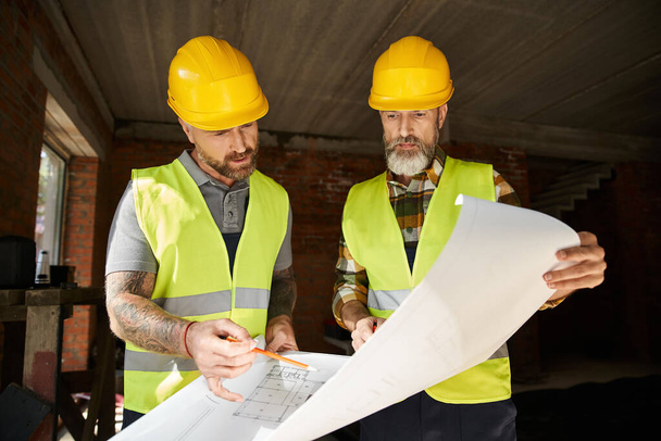 two attractive builders in safety helmets and vests working with blueprint before construction - Photo, Image