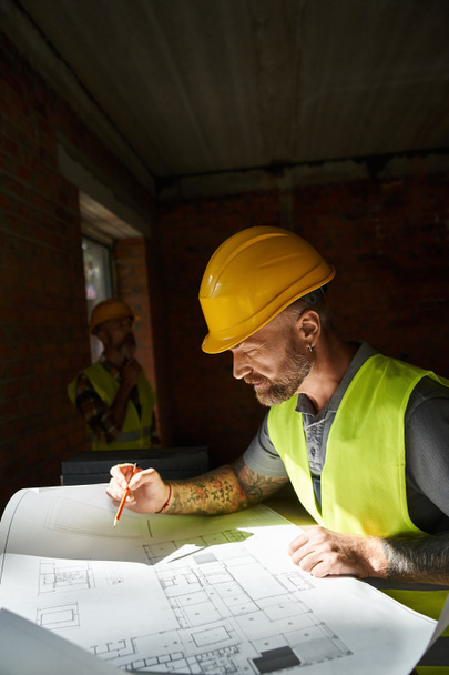 trabajador guapo mirando plano con su colega trabajando en el telón de fondo, constructores de cabañas - Foto, imagen
