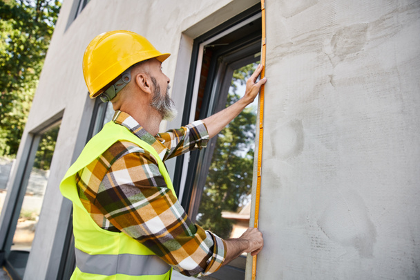 good looking hardworking construction worker with beard measuring window with tape, cottage builder - Photo, Image