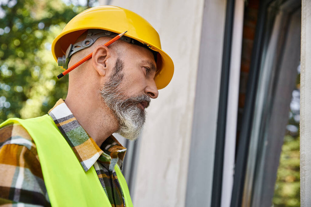 добродушный строитель в защитном шлеме смотрит в окно, находясь на стройке - Фото, изображение