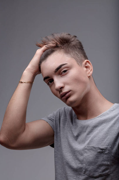 Modebewusster junger Mann mit trendiger Frisur und minimalistischem Sinn für Mode, der sich die Haare von Hand bürstet - Foto, Bild