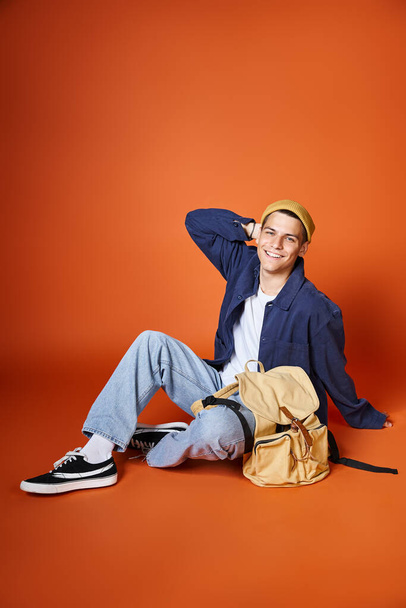 cheerful man in yellow hat sitting with backpack and putting behind head with hand - Photo, Image