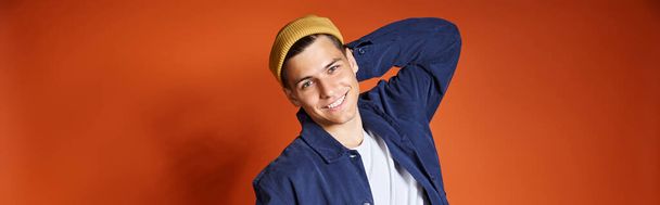 horizontal shot of young man in stylish outfit and yellow hat posing putting hand behind back - Photo, Image