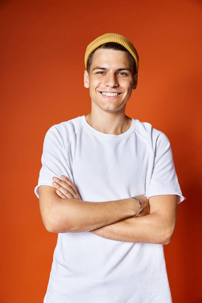 portrait of attractive young man in white t-shirt and yellow hat smiling with arms crossed - Photo, Image