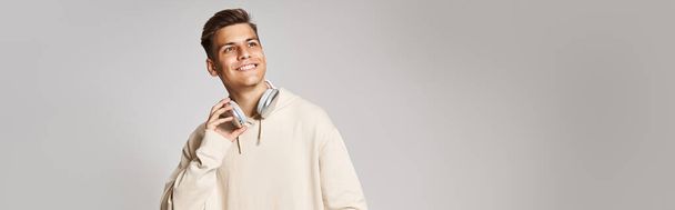 banner of attractive young man in headphones with skateboard looking to up on light background - Photo, Image