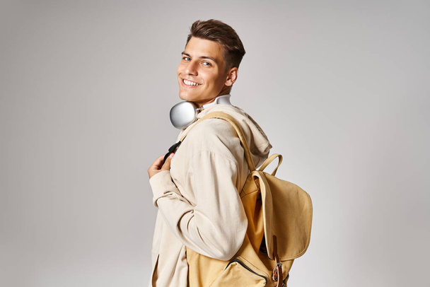 estudiante sonriente en auriculares y atuendo casual con mochila mirando desde atrás - Foto, Imagen