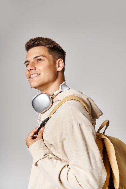 Sırt çantalı, kulaklık takan neşeli bir öğrenci yukarı bakıyor. - Fotoğraf, Görsel